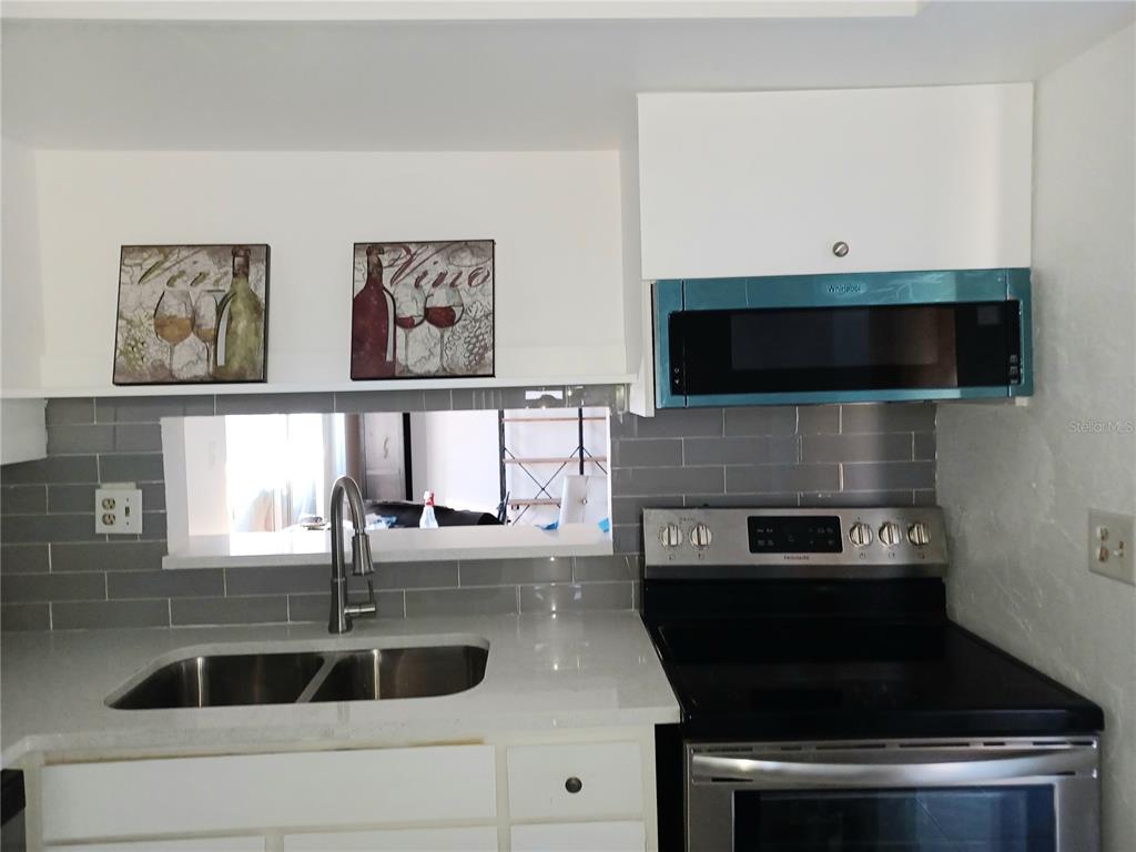 A kitchen features white cabinets, a gray subway tile backsplash, stainless steel appliances, and quartz countertops — 530 CASCADE CIRCLE UNIT 100, CASSELBERRY, FL