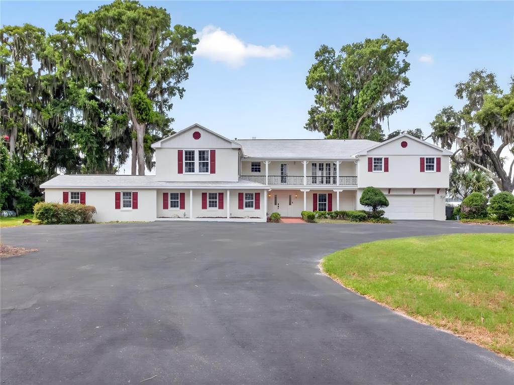 A large two-story house with a white exterior, red shutters, and a wide asphalt driveway — 1029 MELLATHON CIRCLE, LEESBURG, FL