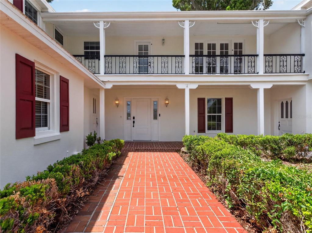 A brick walkway leads to the front entrance of a two-story house with a balcony — 1029 MELLATHON CIRCLE, LEESBURG, FL