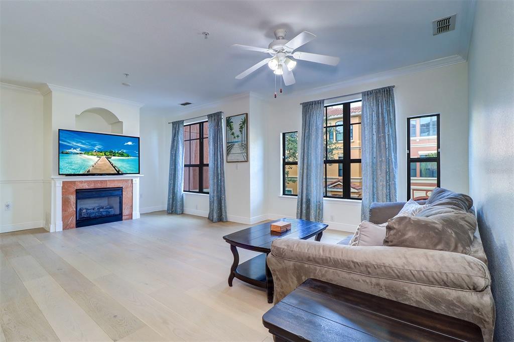 A living room features light wood floors, a fireplace with a television, and large windows — 2741 VIA CIPRIANI UNIT 922B, CLEARWATER, FL