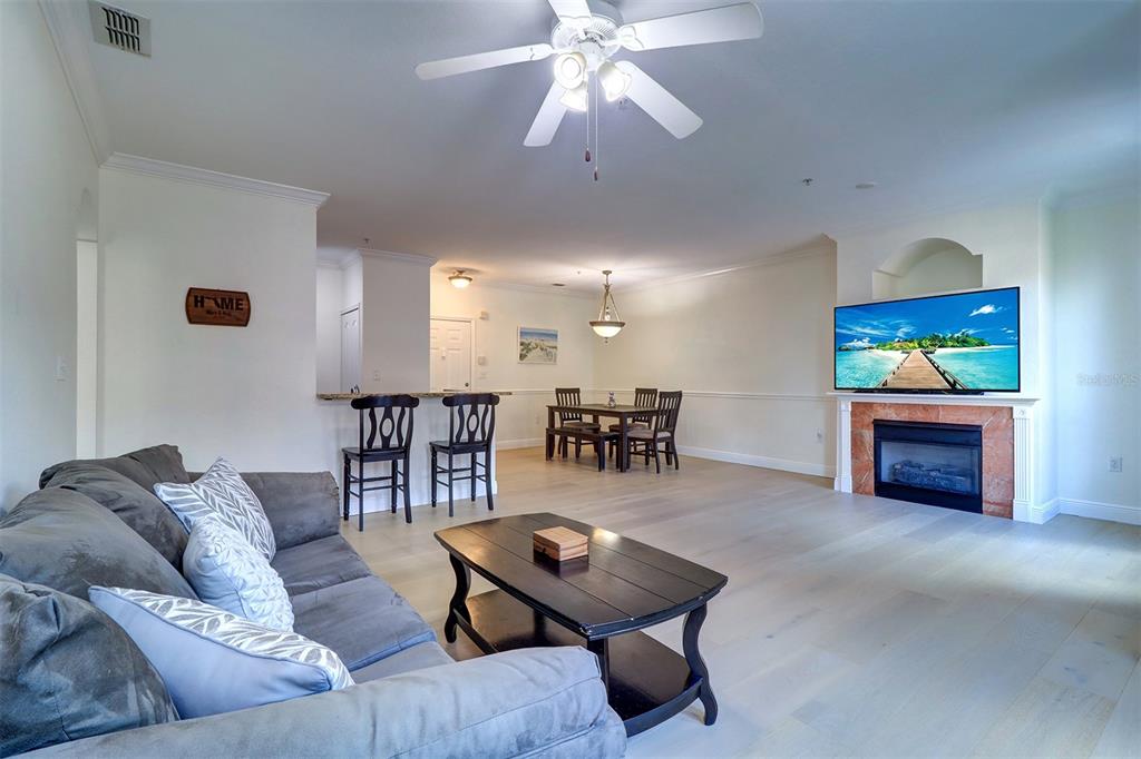 A living room with light wood floors, a fireplace, a ceiling fan, and a dining area — 2741 VIA CIPRIANI UNIT 922B, CLEARWATER, FL