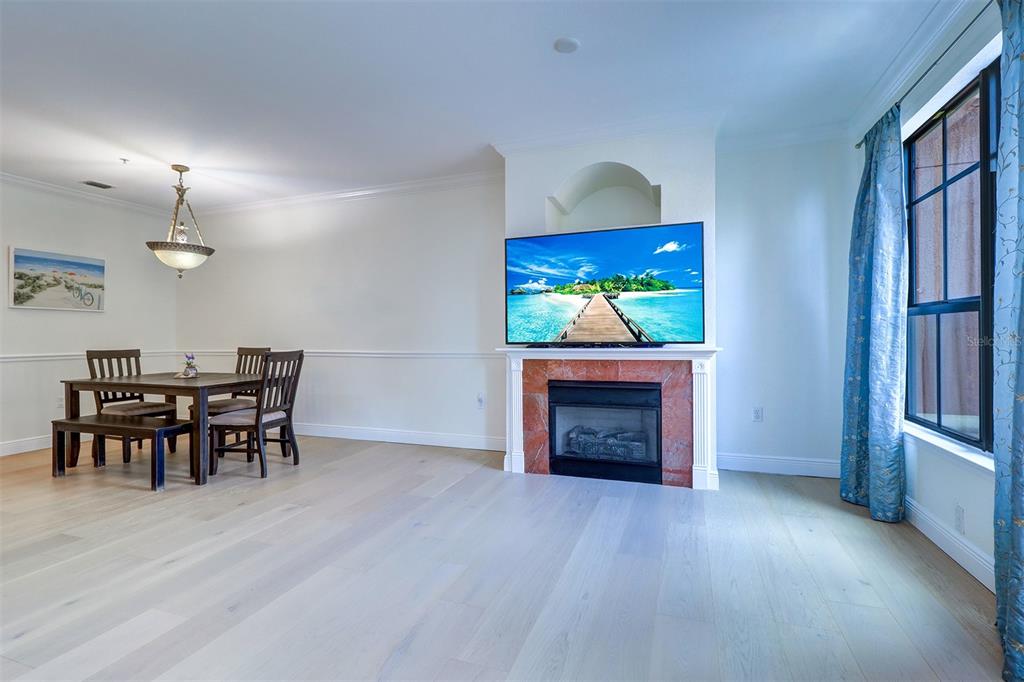 A dining area and living space feature light wood floors, a fireplace, and a television — 2741 VIA CIPRIANI UNIT 922B, CLEARWATER, FL