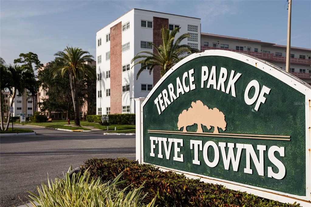 A green sign for Terrace Park of Five Towns stands before a multi-story apartment building — 5980 TERRACE PARK DRIVE N UNIT 108, ST PETERSBURG, FL