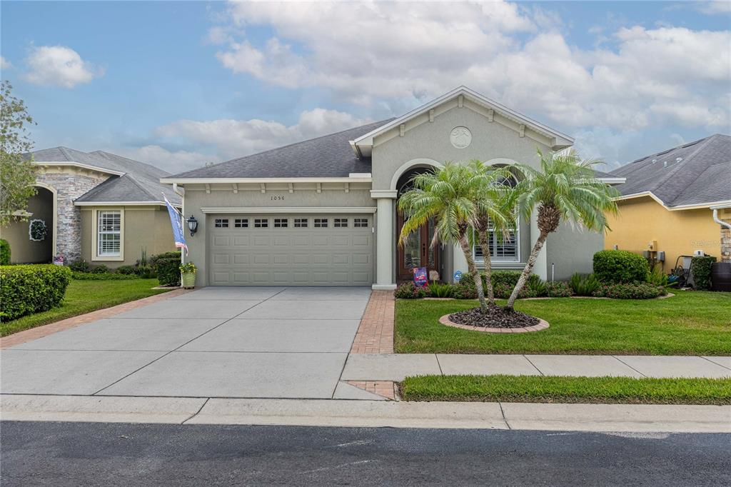 A single-story house with a beige stucco exterior, a two-car garage, and a palm tree — 1056 STONEY CREEK DRIVE, LAKELAND, FL