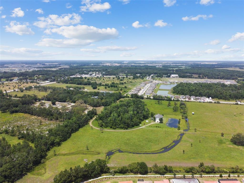 An aerial view shows a rural property with a house, pond, and surrounding green fields — 12345 PARRISH CEMETARY ROAD, PARRISH, FL