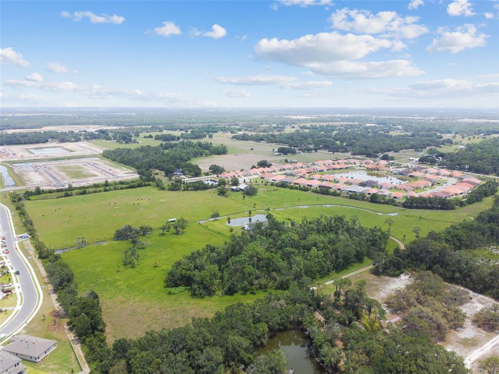 An aerial view shows a large grassy field, a small pond, and nearby residential developments — 12345 PARRISH CEMETARY ROAD, PARRISH, FL