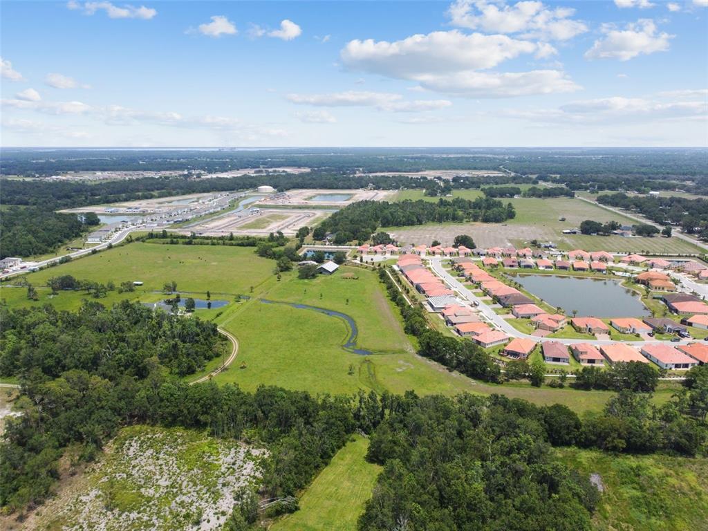 An aerial view shows a residential neighborhood with a pond adjacent to open green fields — 12345 PARRISH CEMETARY ROAD, PARRISH, FL