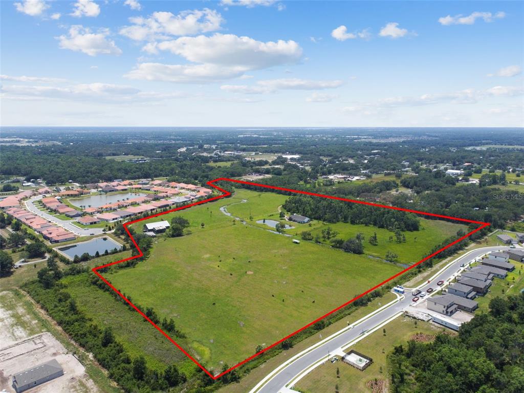 An aerial view shows a large, fenced grassy pasture bordered by residential developments and trees — 12345 PARRISH CEMETARY ROAD, PARRISH, FL