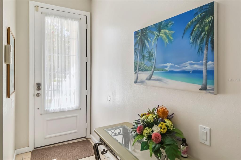 An entryway features a white door with a glass insert, a beach-themed painting, and a console table — 2382 SILVER PALM DRIVE E, KISSIMMEE, FL