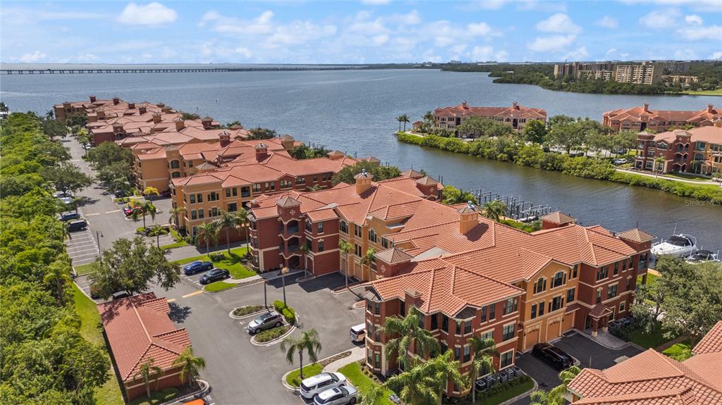 An aerial view shows multi-story Mediterranean-style apartment buildings with red tile roofs near a bay — 2741 VIA CIPRIANI UNIT 916A, CLEARWATER, FL