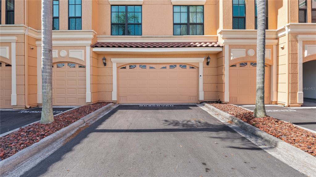 An exterior view of a multi-story building featuring three garage doors and palm trees — 2741 VIA CIPRIANI UNIT 916A, CLEARWATER, FL