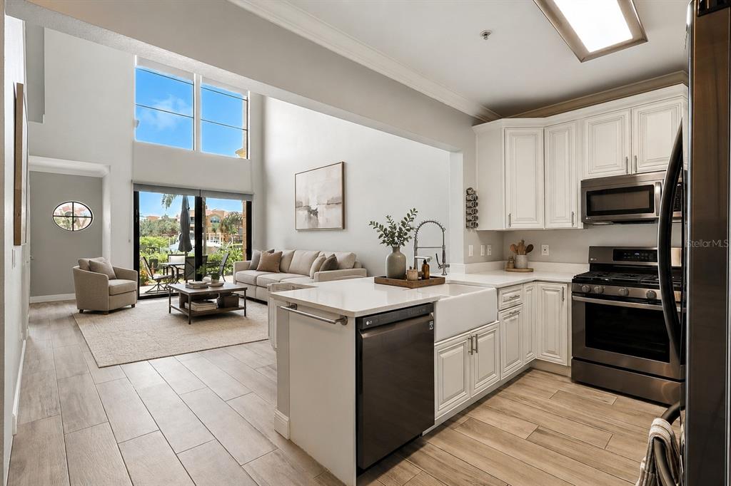 A kitchen with white cabinets and stainless steel appliances overlooks a living area with high ceilings — 2741 VIA CIPRIANI UNIT 916A, CLEARWATER, FL