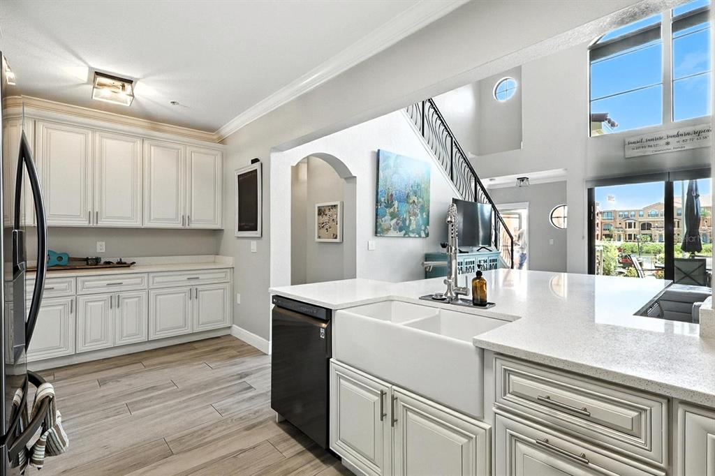 A kitchen with white cabinets, a farmhouse sink, and light wood-look flooring — 2741 VIA CIPRIANI UNIT 916A, CLEARWATER, FL