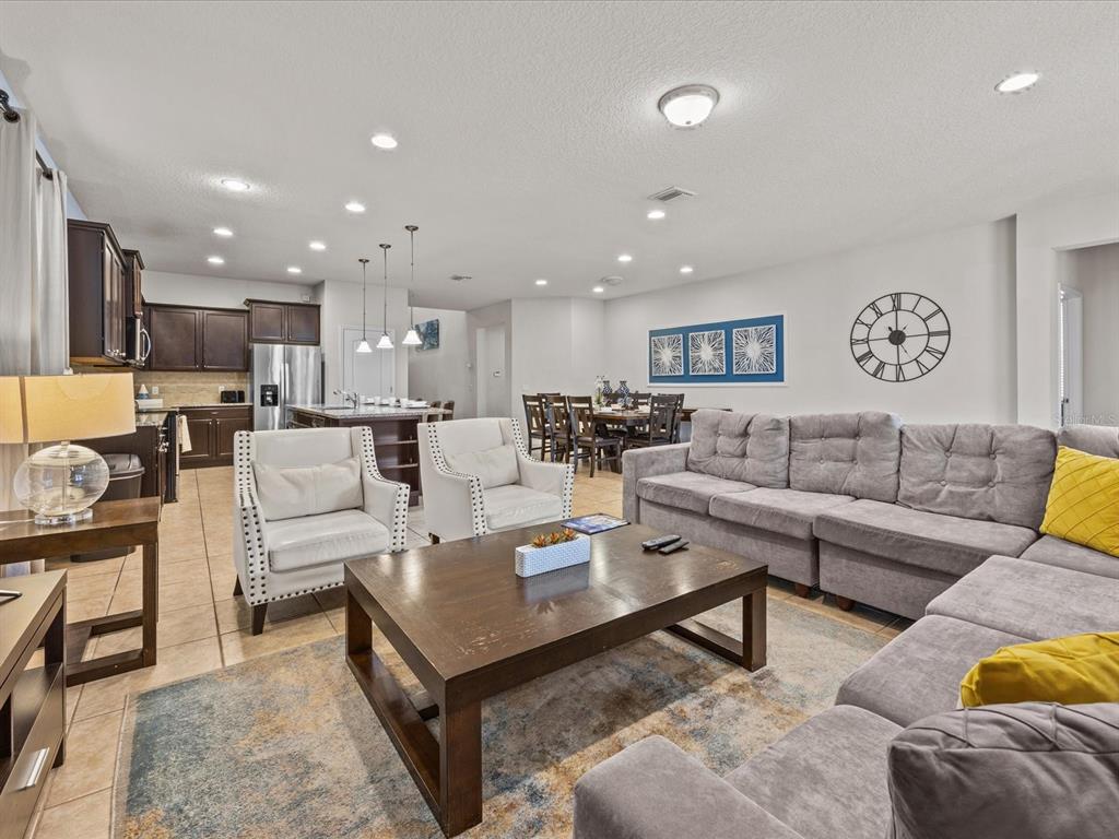 An open-concept living room features a gray sectional, two white armchairs, and a kitchen area — 8832 MACAPA DRIVE, KISSIMMEE, FL