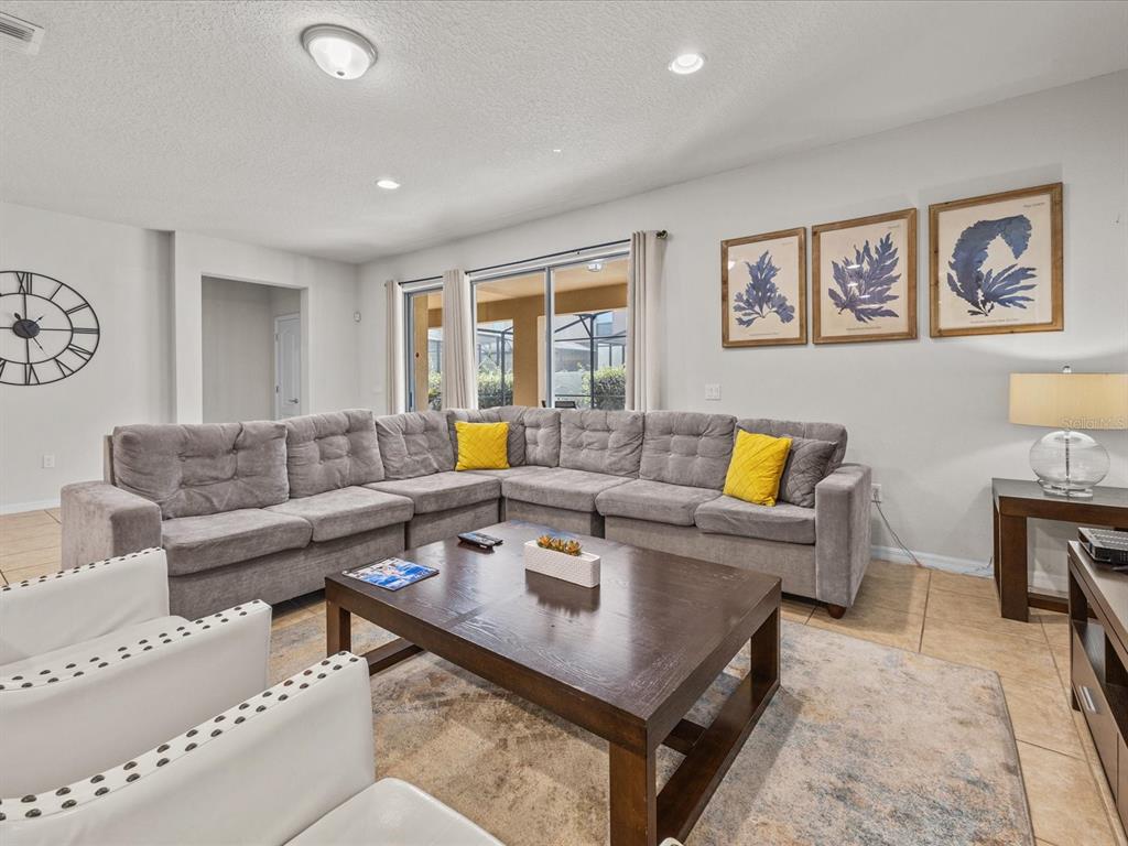 A living room features a large gray sectional sofa, a dark wood coffee table, and wall art — 8832 MACAPA DRIVE, KISSIMMEE, FL