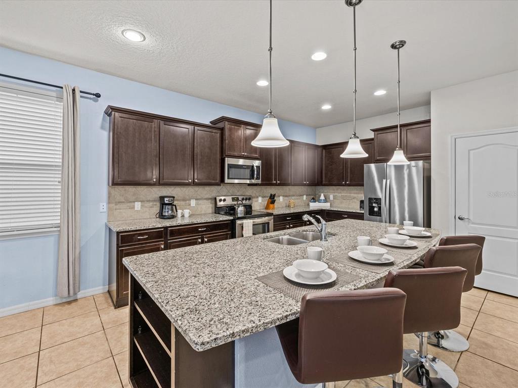 A kitchen features dark wood cabinets, granite countertops, a large island, and three pendant lights — 8832 MACAPA DRIVE, KISSIMMEE, FL