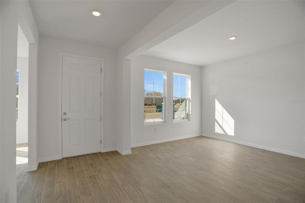 An empty room features white walls, wood-look tile flooring, recessed lighting, and two windows — 2371 JUNIPER BERRY DRIVE, MINNEOLA, FL