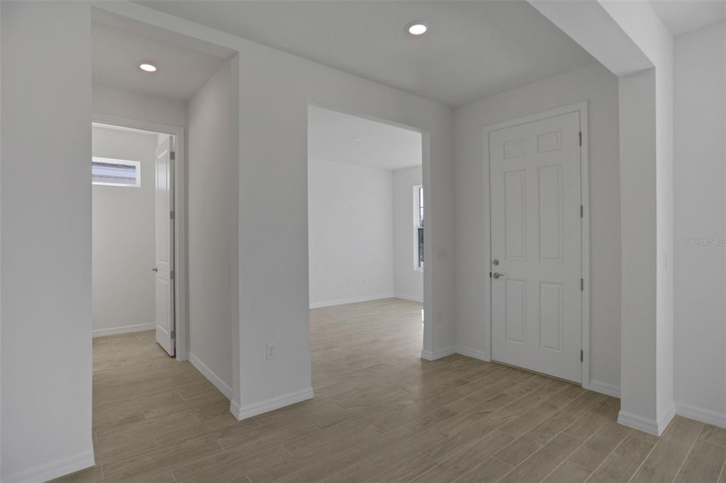 A bright entryway with light wood-look tile flooring leads to an adjacent room and doorway — 2371 JUNIPER BERRY DRIVE, MINNEOLA, FL