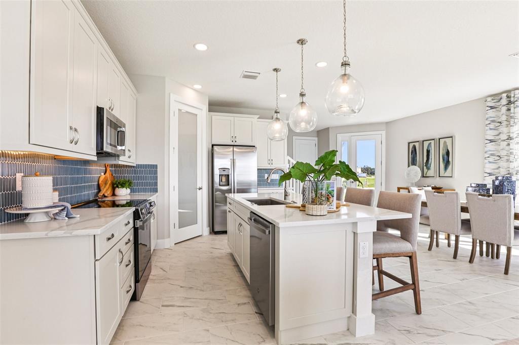 A modern kitchen features white cabinets, a central island with seating, and blue tile backsplash — 31493 SPANISH MISSION ROAD, SAN ANTONIO, FL