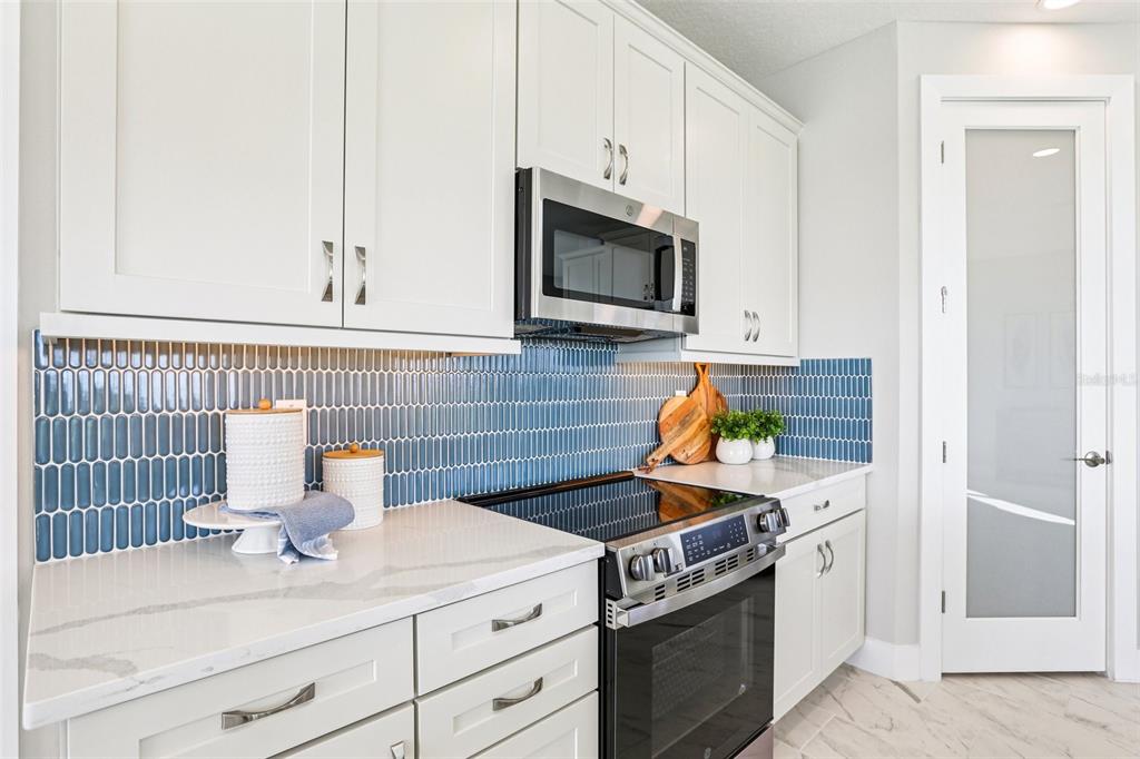 A kitchen features white cabinets, a blue tile backsplash, stainless steel appliances, and quartz countertops — 31493 SPANISH MISSION ROAD, SAN ANTONIO, FL
