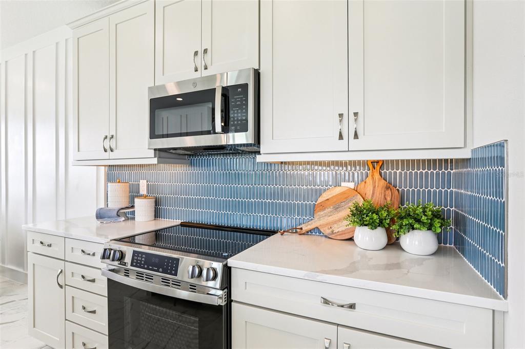 A kitchen features light gray cabinets, a stainless steel microwave, and a blue picket-tile backsplash — 31493 SPANISH MISSION ROAD, SAN ANTONIO, FL