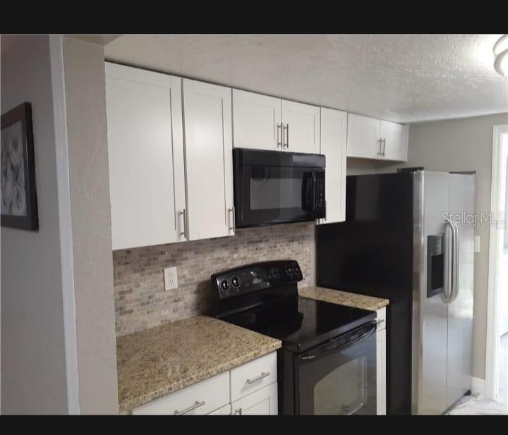 A kitchen features white cabinets, granite countertops, a black stove, a microwave, and stainless refrigerator — 3602 N 55TH STREET, TAMPA, FL