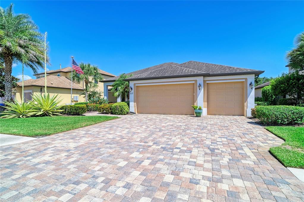 A single-story house with a three-car garage and a paved driveway under a clear sky — 517 CHANTILLY TRAIL, BRADENTON, FL