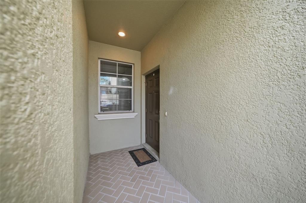 A covered entryway features a brown door, a window, and light-colored herringbone tile flooring — 9484 TRUMPET VINE LOOP, TRINITY, FL
