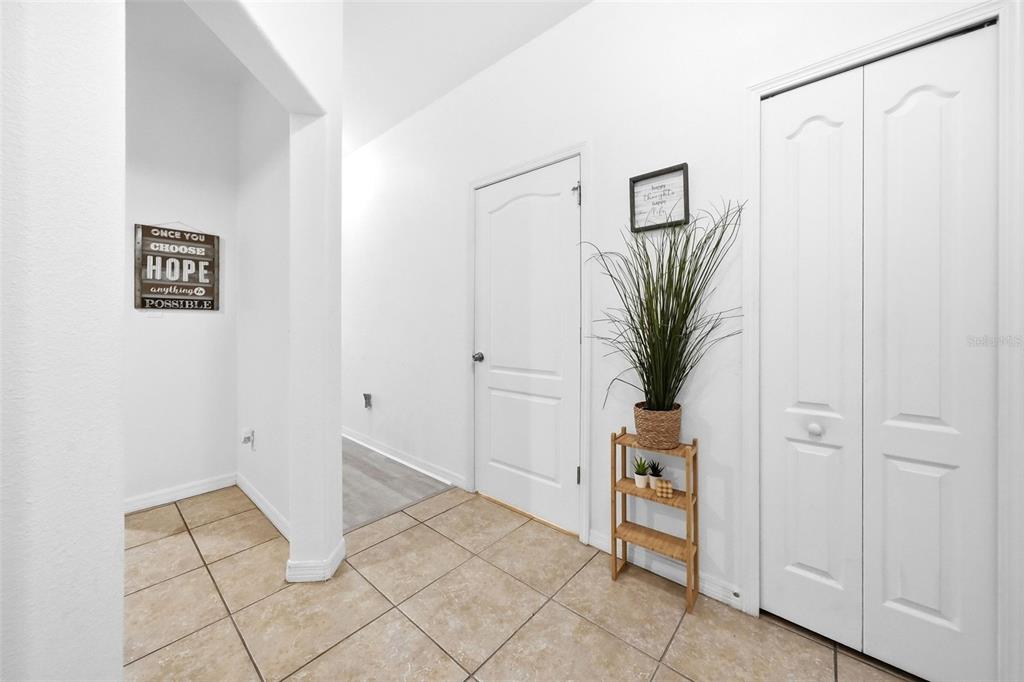 A tiled hallway features a white door, a closet, and a small wooden plant stand — 9484 TRUMPET VINE LOOP, TRINITY, FL