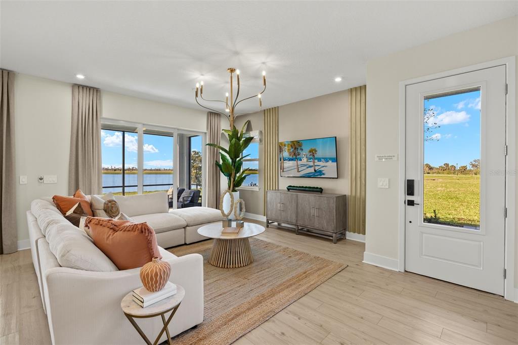 A bright living room features a sectional sofa, a television, and large windows overlooking water — 12766 JADE EMPRESS LOOP UNIT 101, VENICE, FL