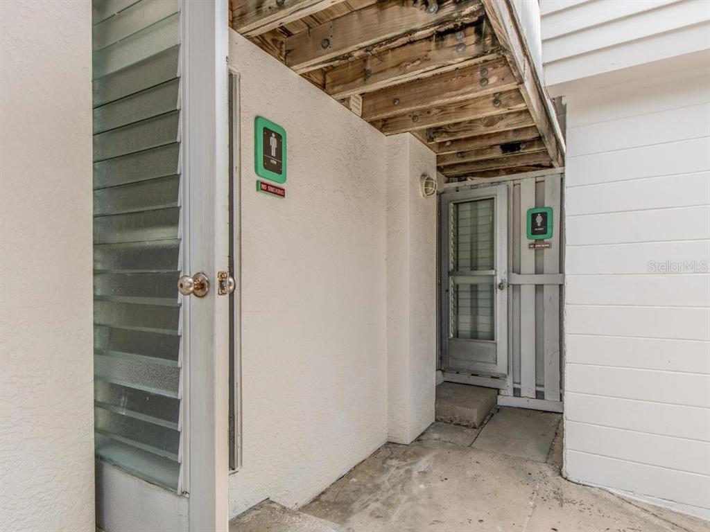 A concrete walkway leads to a doorway and a screened door with restroom signage — 200 WINDWARD PASSAGE UNIT 66, CLEARWATER BEACH, FL