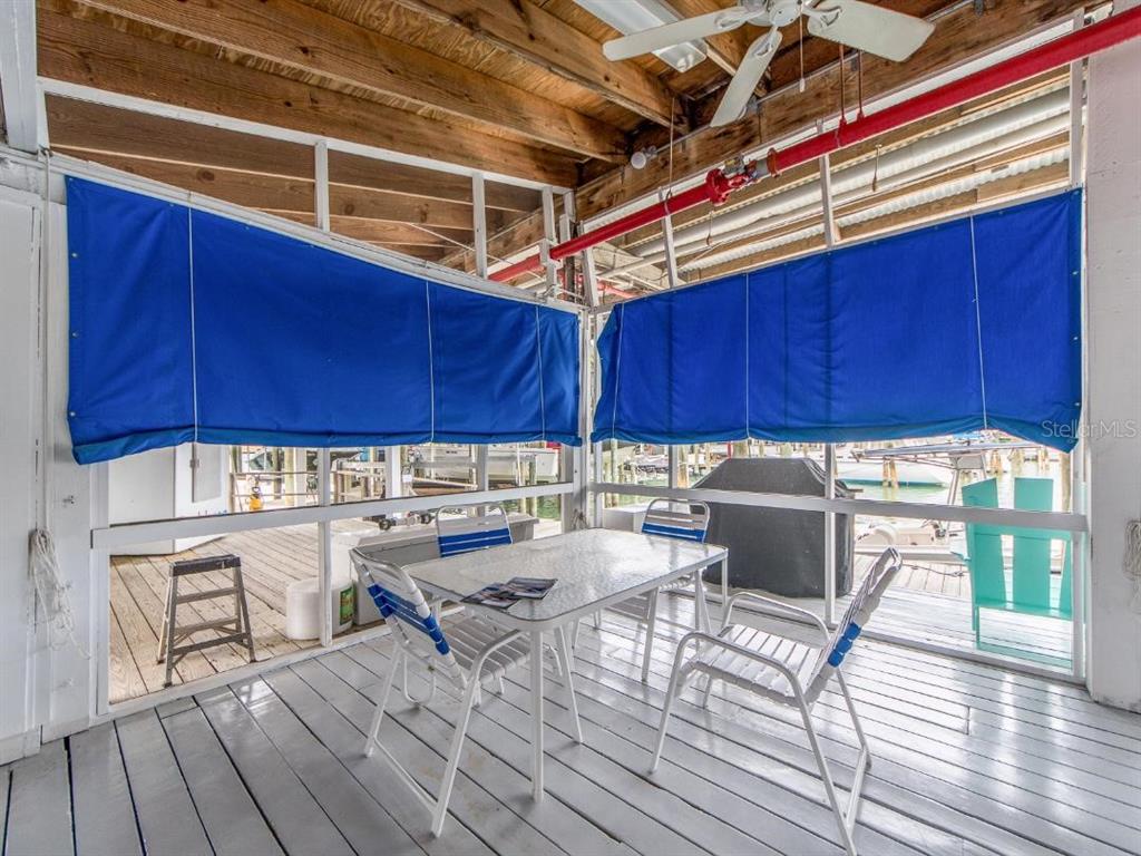 A screened-in porch features a dining set, blue privacy shades, and a view of boats — 200 WINDWARD PASSAGE UNIT 66, CLEARWATER BEACH, FL