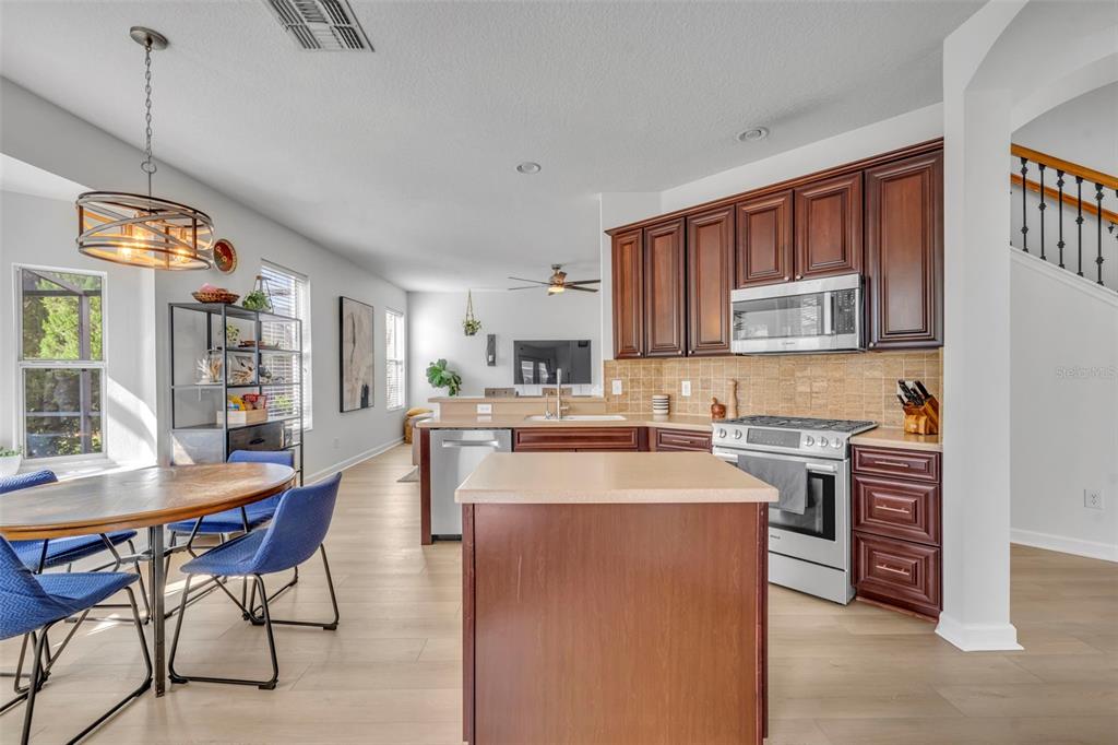 A kitchen with dark wood cabinets, stainless steel appliances, and an island faces a dining area — 2329 NATOMA BLVD, MOUNT DORA, FL