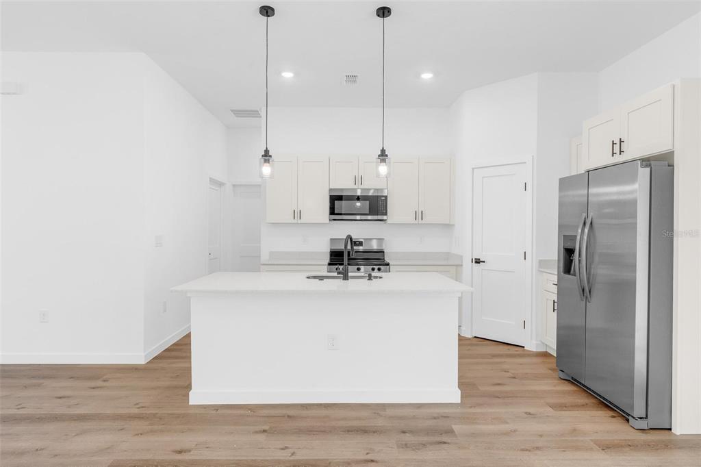 A modern kitchen features white cabinetry, a central island, stainless steel appliances, and wood flooring — 10615 N DIDISCUS DRIVE, CITRUS SPRINGS, FL