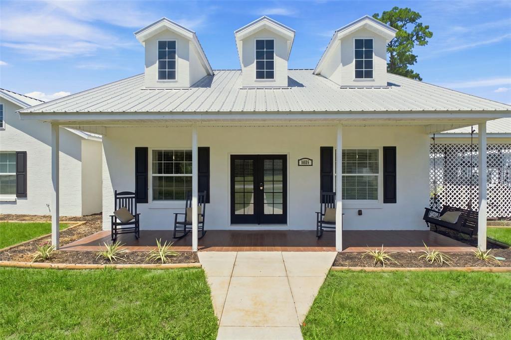 A white house with a metal roof, three dormers, and a front porch with rocking chairs — 10574 N SUNFLOWER POINT, CRYSTAL RIVER, FL
