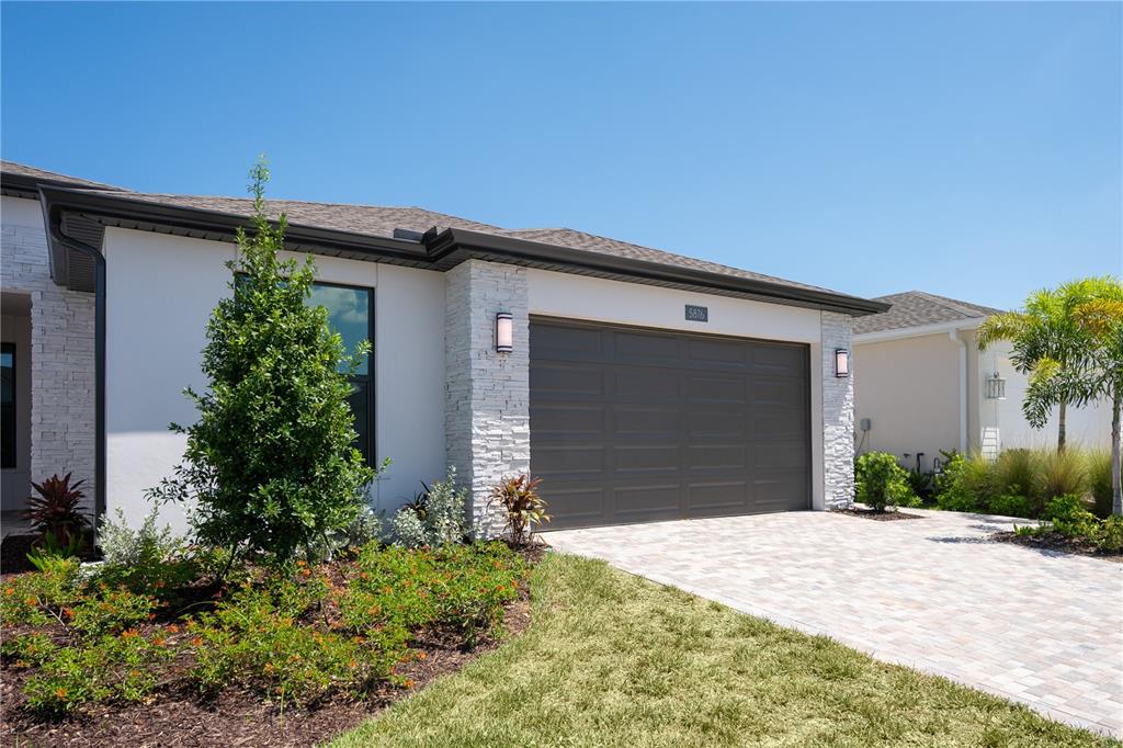 A modern house exterior features a stone facade, white walls, and a dark garage door — 5876 WINDBREAK COURT, APOLLO BEACH, FL
