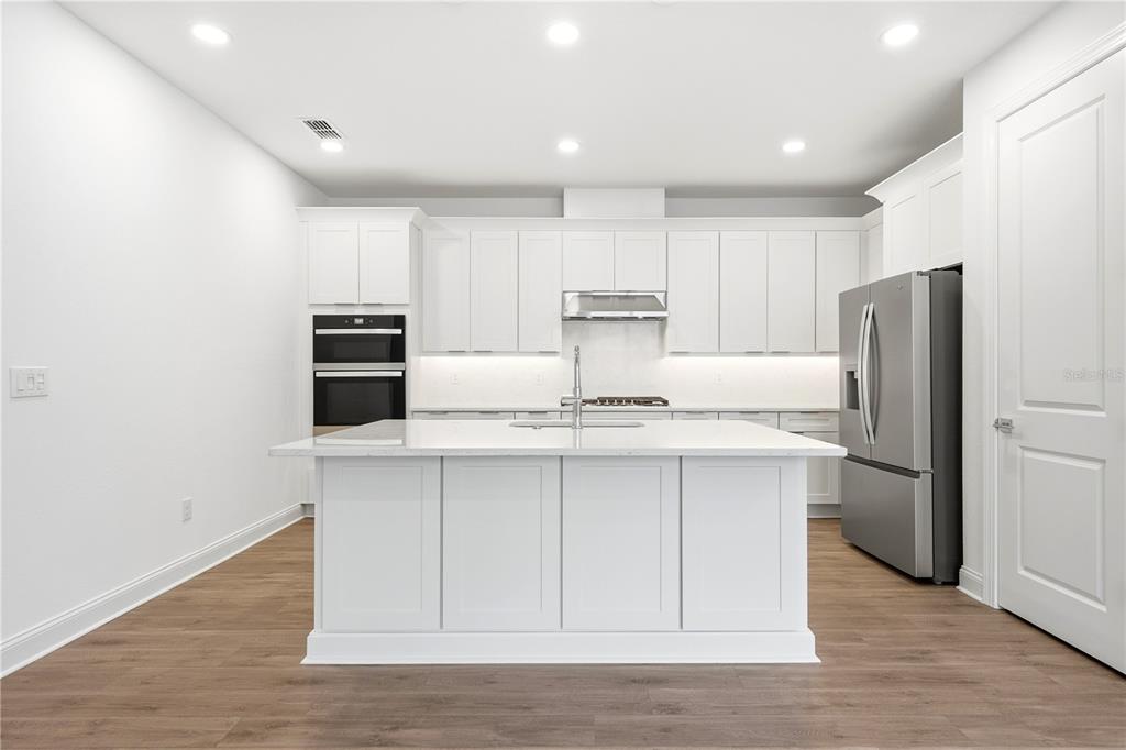 A modern kitchen features white cabinetry, a central island, stainless steel appliances, and wood flooring — 5876 WINDBREAK COURT, APOLLO BEACH, FL