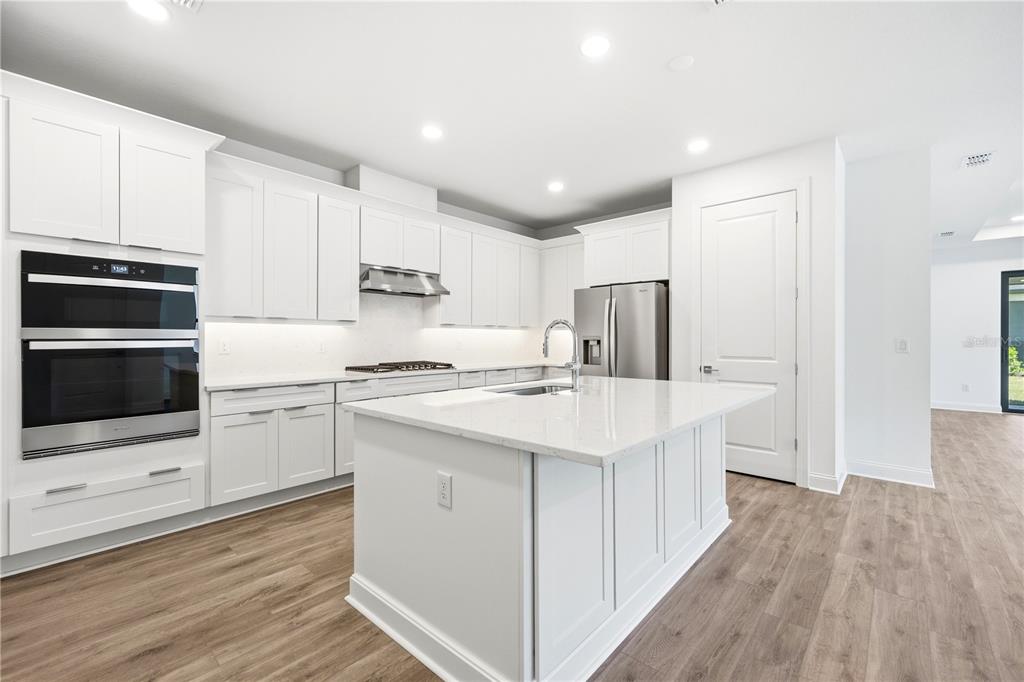 A modern kitchen features white cabinetry, stainless steel appliances, a center island, and wood flooring — 5876 WINDBREAK COURT, APOLLO BEACH, FL