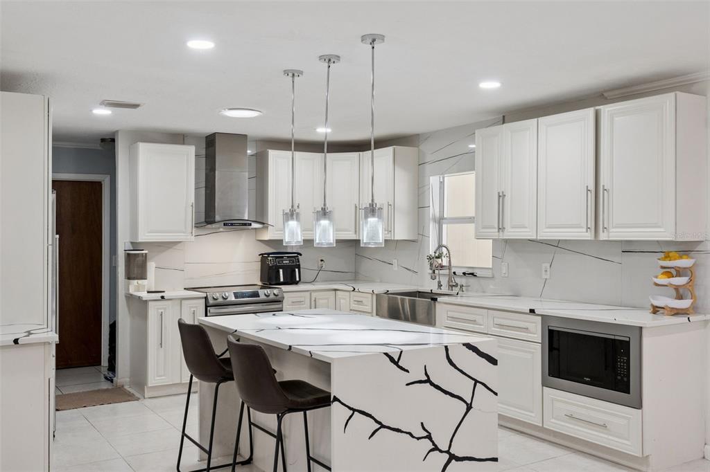 A modern kitchen features white cabinets, a marble-patterned island with seating, and stainless steel appliances — 1756 TANGLEWOOD DRIVE, KISSIMMEE, FL