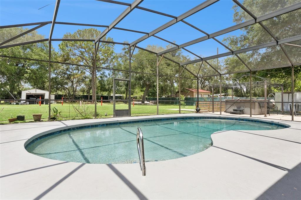 A swimming pool enclosed by a screened lanai overlooks a large, grassy backyard with trees — 1756 TANGLEWOOD DRIVE, KISSIMMEE, FL