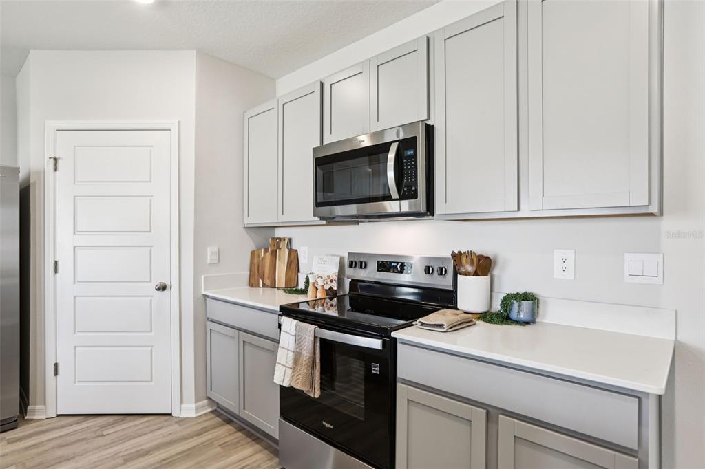 A kitchen features light gray cabinets, stainless steel appliances, and white countertops — 148 FLAG LILLY LANE, UMATILLA, FL