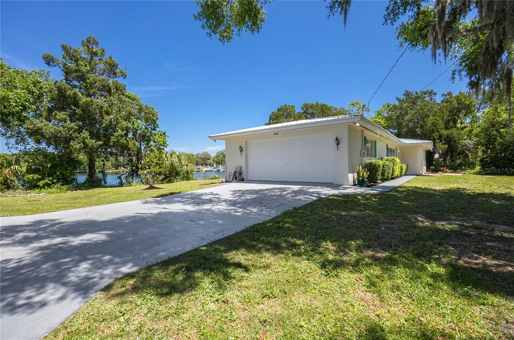 A white, single-story house with a two-car garage sits on a grassy, waterfront lot — 3861 N RINGDOVE POINT, CRYSTAL RIVER, FL