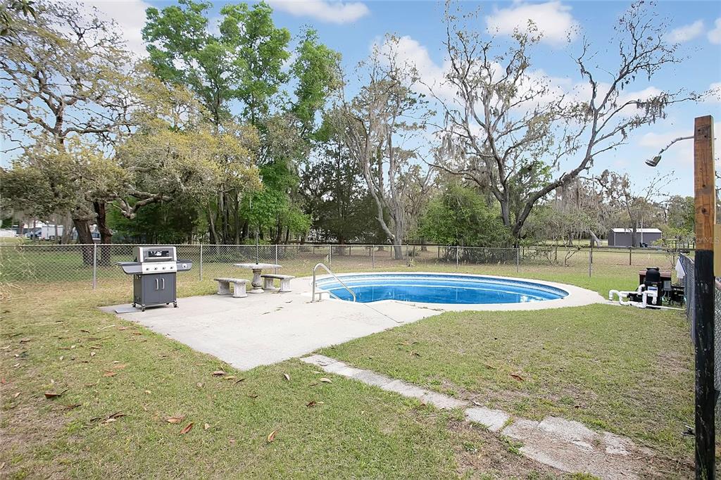 An outdoor backyard features a swimming pool, a concrete patio, a grill, and mature trees — 3116 E BUCK, INVERNESS, FL