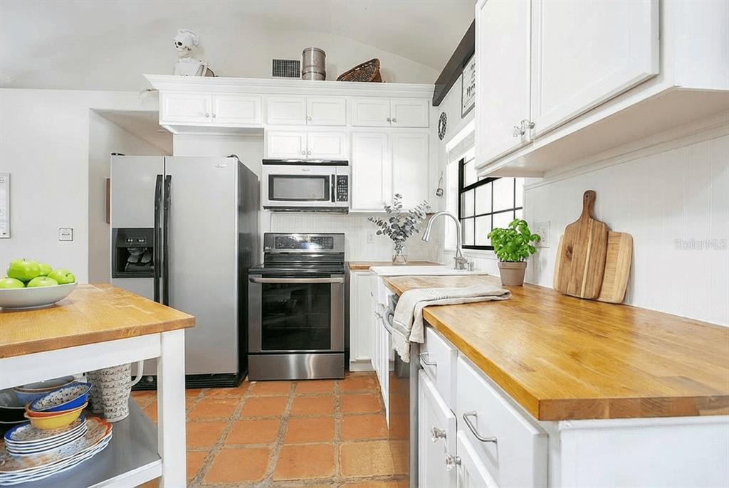 A kitchen features white cabinets, butcher block countertops, stainless steel appliances, and terracotta tile flooring — 3116 E BUCK, INVERNESS, FL