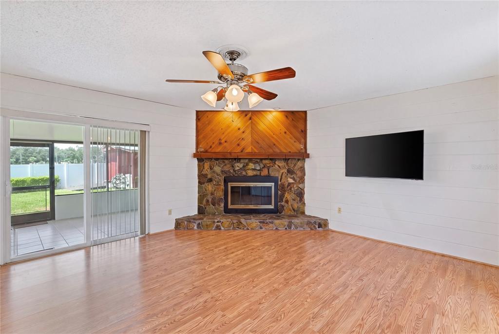 A living room features a stone corner fireplace, wood paneling, and a sliding glass door — 1105 LENNA AVENUE, SEFFNER, FL