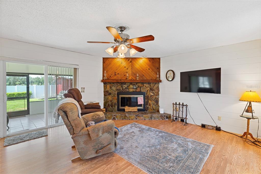 A living room features a stone fireplace, wood-paneled accent wall, ceiling fan, and sliding glass doors — 1105 LENNA AVENUE, SEFFNER, FL