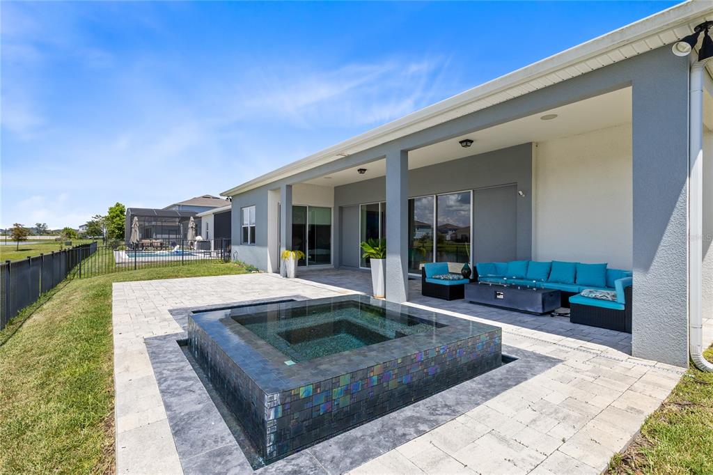 A backyard patio features a tiled square spa, a covered seating area, and a black fence — 13828 TYBEE BEACH LANE, ORLANDO, FL