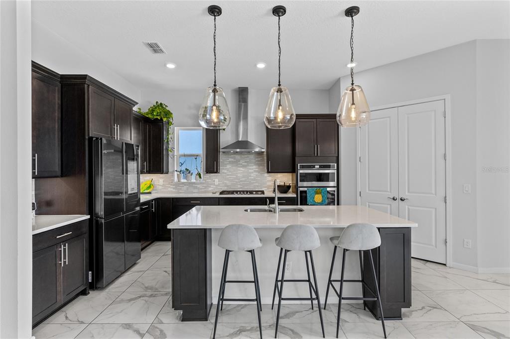 A modern kitchen features dark cabinetry, a white quartz island with three stools, and pendant lighting — 13828 TYBEE BEACH LANE, ORLANDO, FL