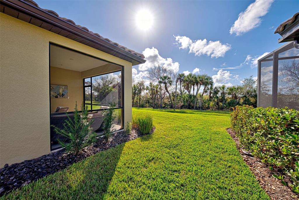 A view of a screened-in patio and a grassy backyard with palm trees — 233 PALIDORO CIRCLE, NOKOMIS, FL