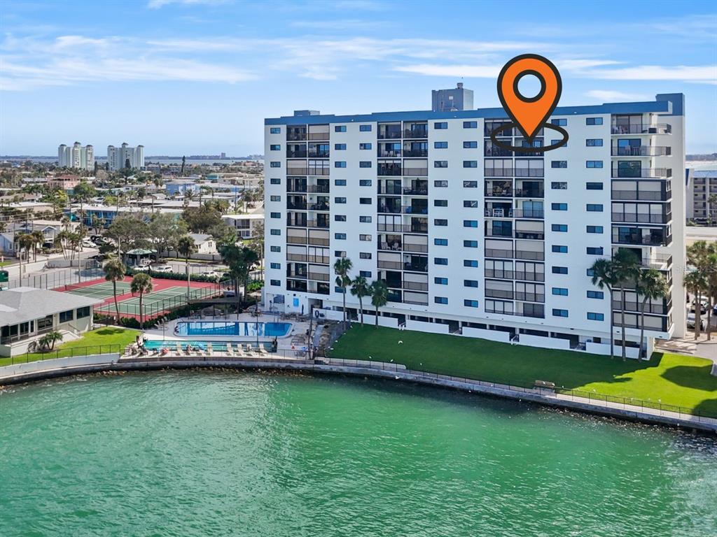 An aerial view of a multi-story waterfront apartment building with a pool and tennis courts — 7150 SUNSET UNIT 903E, ST PETE BEACH, FL